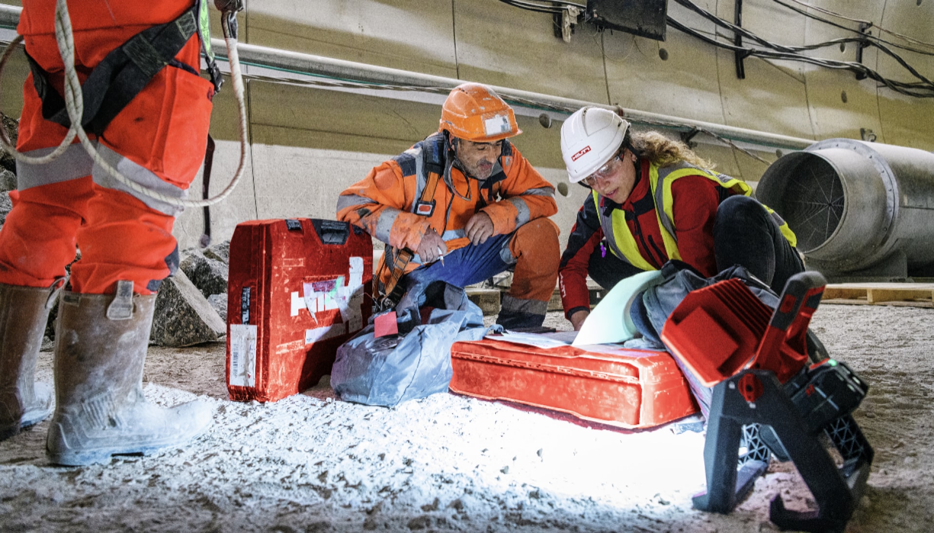 Hilti Account Manager on subway construction site kneeling on dirt floor, checking documents with customer